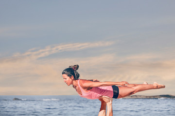 Young sporty woman practicing acroyoga at sunrise or sunset.
