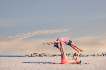 Fototapeta na wymiar Young sporty couple practicing acroyoga exercises at sunrise or sunset.