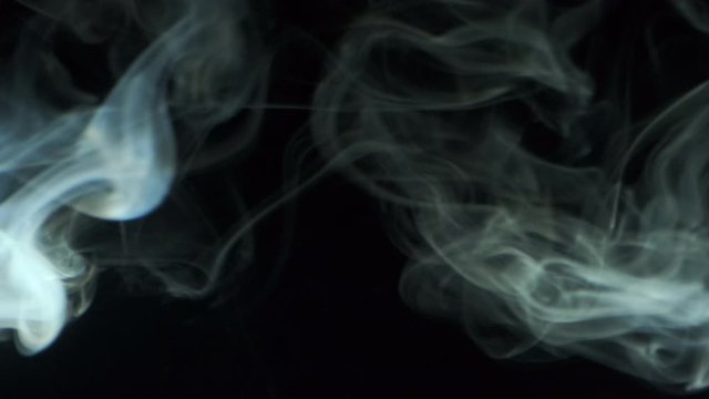 Vertical video screensaver - Trickle silvery smoke slowly rising graceful twists upward. Cigar smoke blowing from the left side. Closeup, isolated on black background.