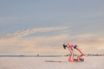 Young sporty couple practicing acroyoga exercises at sunrise or sunset.