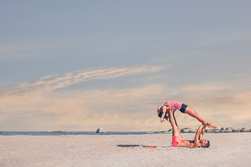 Young sporty couple practicing acroyoga exercises at sunrise or sunset.