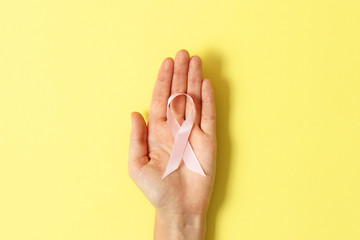 Pink ribbon in hands on a colored background. International Breast Cancer Sign.