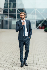 Full length photo of a young business man unbuttoning the jacket of his suit while looking away from the camera