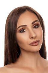 Fototapeta premium Close up portrait of a brunette nude model girl with professional evening make-up and plump lips, posing isolated on white background.