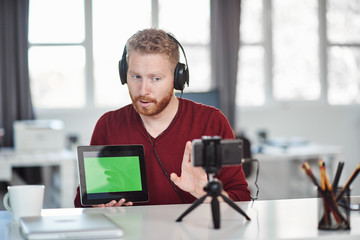 Handsome Caucasian employee having presentation over the internet. In hands is tablet and on head are headphones. Start up business concept.
