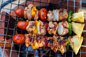Skewers with pieces of grilled barbecue, green bell pepper, red tomato and meat for sell in street market, Thailand, closeup