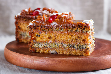 a piece of cake with caramel cream and poppy seeds on a wooden kitchen board, white background..