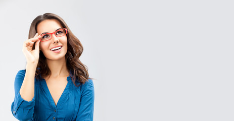 Portrait of happy smiling young cheerful business woman, in eye glasses, looking up, isolated over grey color background, with blank copy space place for some text