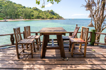 Wooden table and chairs in empty beach cafe next to sea water. Island Koh Phangan, Thailand