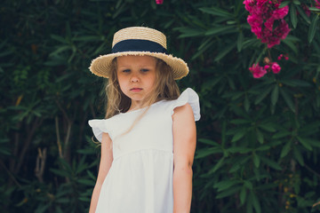 cute girl in white dress and hat posing in blooming flowers