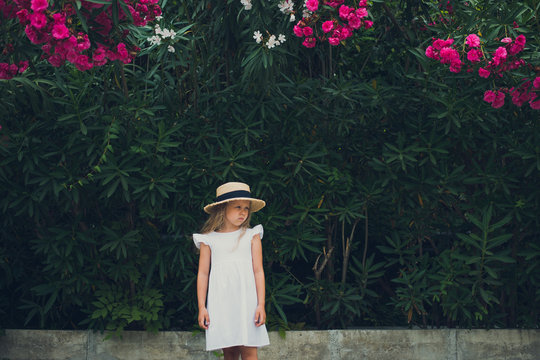 cule girl in white dress and hat posing in blooming flowers