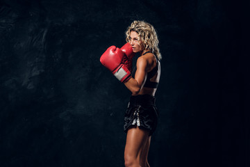 Sportive muscular woman is demonstrating her boxing exercises, wearing gloves.