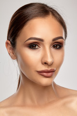 Close up portrait of a brunette nude model girl with professional evening make-up and plump lips, posing on gray background.