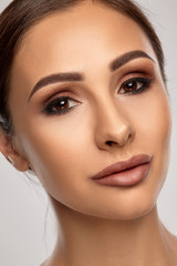 Close up portrait of a brunette nude model girl with professional evening make-up and plump lips, posing on gray background.