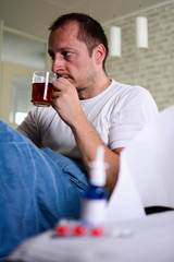 healthcare, people and medicine concept - ill man with flu coughing and drinking hot tea from cup at home