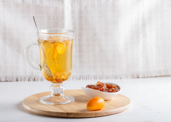 Jasmine tea with kumquat in a glass cup on a wooden board on a white background.