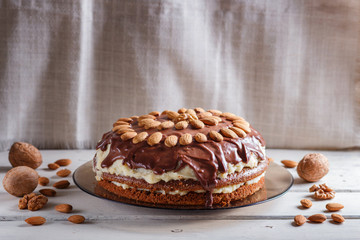 Homemade chocolate cake with milk cream and almonds on white wooden background.