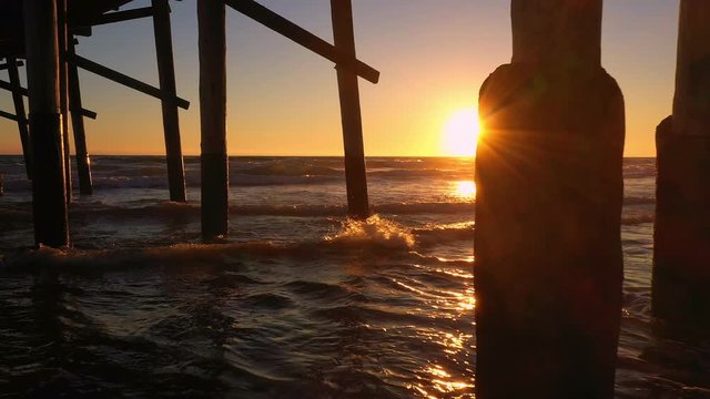 Flying under Newport Beach pier at sunset as waves roll into the beach in California.