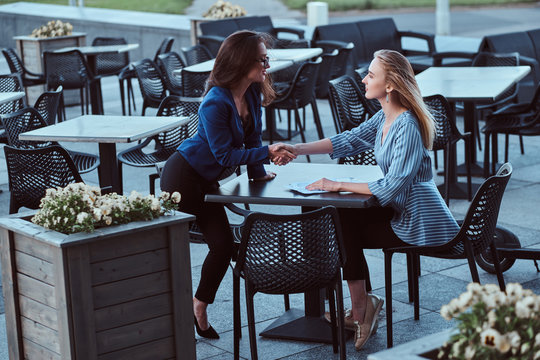 Two cooperative workers are disscussing new project outside office, at caffeteria at nice summer day.