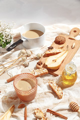 Coffee with milk, cookies, cinnamon and fruits on the tablecloth.