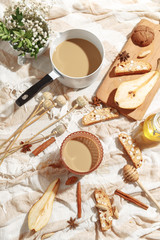 Coffee with milk, cookies, cinnamon and fruits on the tablecloth.