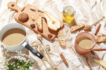 Coffee with milk, cookies, cinnamon and fruits on the tablecloth.