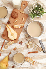 Coffee with milk, cookies, cinnamon and fruits on the tablecloth.