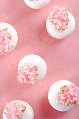Minimalistic composition with bunch of white french macaron sweets with pink crystal shaped marmalade decoration over grunged concrete texture background. Top view, close up, flat lay, copy space.