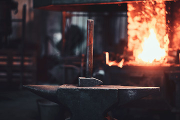 Hammer on anvil at dark blacksmith workshop with fire in stove at background. - obrazy, fototapety, plakaty