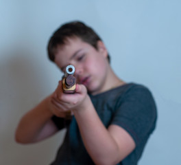 close - up of the dangerous front edge of a toy gun. Despite the fact that the depth of field is extremely small, in the background you can see the vague figure of a teenager with a gun in his hands.