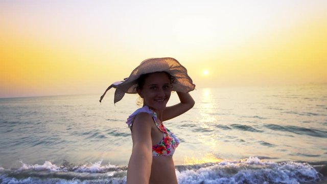 Romantic couple on honeymoon at sunset. Smiling girlfriend with hat walking with holding hand of her boyfriend on the beach. Couple enjoying summer vacation on beach