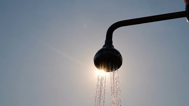 Shower head water drops backlit by summer sun, slow motion