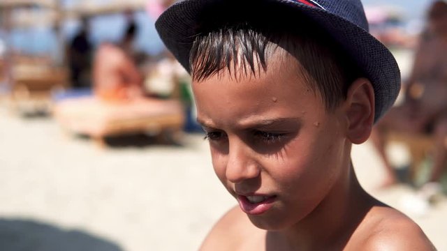 Handsome boy with hat look at camera and smile sitting on beach, cinematic dof