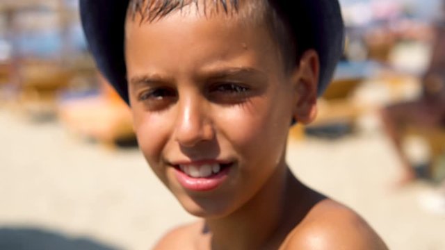 Happy hispanic boy with hat smiling on beach and give a kiss to camera