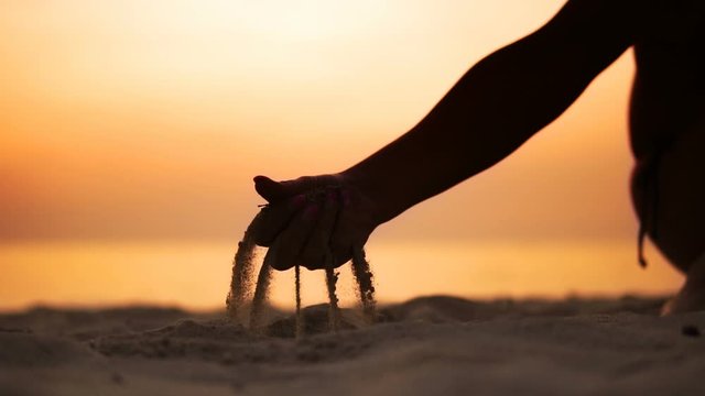 Silhouette hand releasing dropping sand. Sand flowing through the hands against orange ocean sunset. Summer beach holiday vacation concept, SLOW MOTION
