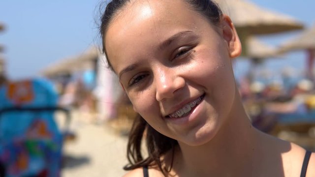 Beautiful happy teen girl with tooth braces smiling to camera sitting on beach during summer vacation