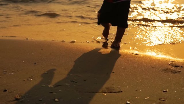 Mother and child walking on a sandy beach at sunset splashed by sea waves, SLOW MOTION