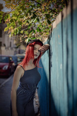 Obraz premium Young fashionable woman in clothes in a strip and red hair, posing on a blue background on the street.