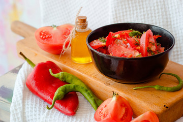 Still life tomato and pepper salad in bowl and oil in jar on white drapery of waffle towel on pink background