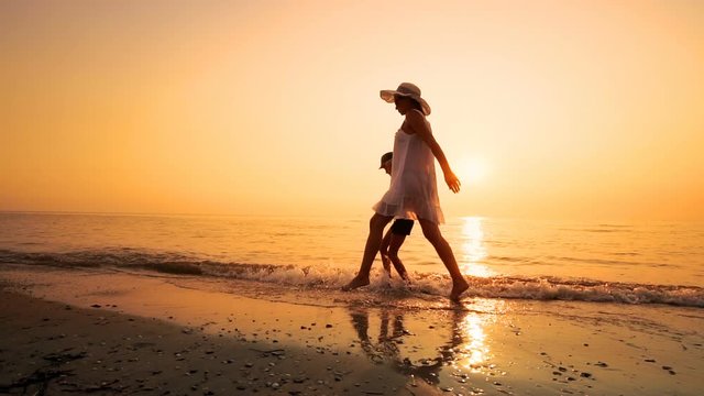 Happy family walking on empty ocean beach at sunset, SLOW MOTION