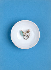 Woman's jewelry like gold rings in a decorative bowl isolated on blue background. Flat lay. Top view. Copy space