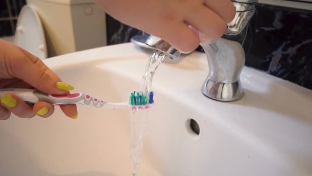 Cleaning, washing a toothbrush over the clean white sink and tap, slow motion