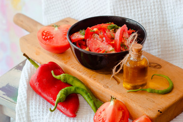 Still life tomato and pepper salad in bowl and oil in jar on white drapery of waffle towel on pink background