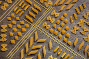 abstract flatlay from farfalle penne fusilli, many different types of pasta, dry pasta, geometric pattern on a stone table, traditional Italien food