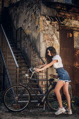 Fototapeta na wymiar Young girl in mini shorts and glasses is parking her bicycle at evening near her house.