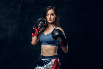Portrait of serious female boxer in boxing gloves and sportive wear at dark photo studio.
