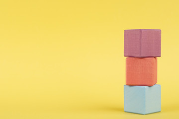 Colored wooden cubes on yellow background, children education