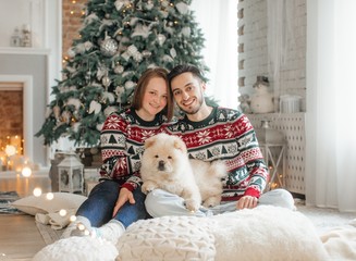 Beautiful new-year portrait of the young falling in love together with the dog of чаучау in Christmas decorations