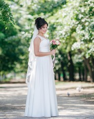 Fototapeta na wymiar Beautiful bride with stylish make-up in white dress in spring garden 