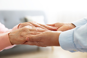 Mature female in elderly care facility gets help from hospital personnel nurse. Senior woman w/ aged wrinkled skin & care giver, hands close up. Grand mother everyday life. Background, copy space.